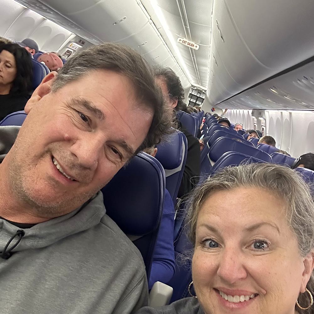 John and Jacque smiling over the seat backs on a plane.