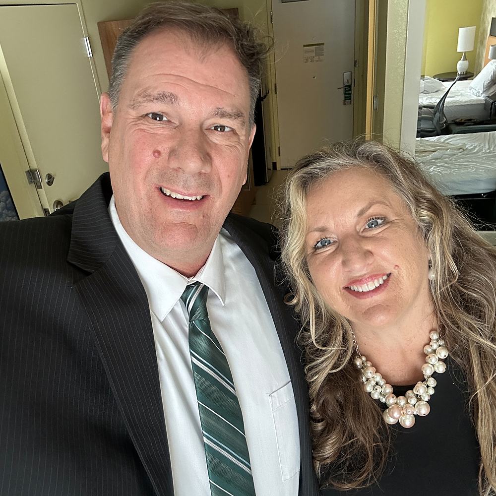 John in a suit and Jacque in pearls, dressed up and smiling.